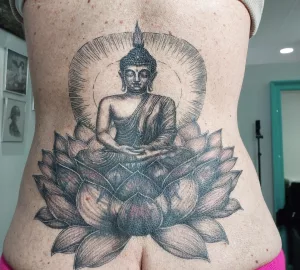 Nahaufnahme eines Rücken-Tattoos. Das Tattoo ist ein Cover-up und zeigt einen Buddha in einer groq Lotusblüte.