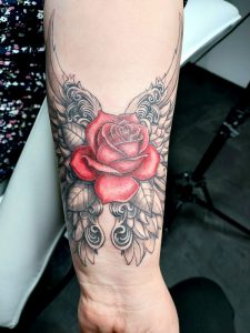 Unterarm-Tattoo in Farbe und black and grey, rote Rose mit Engelsflügeln.