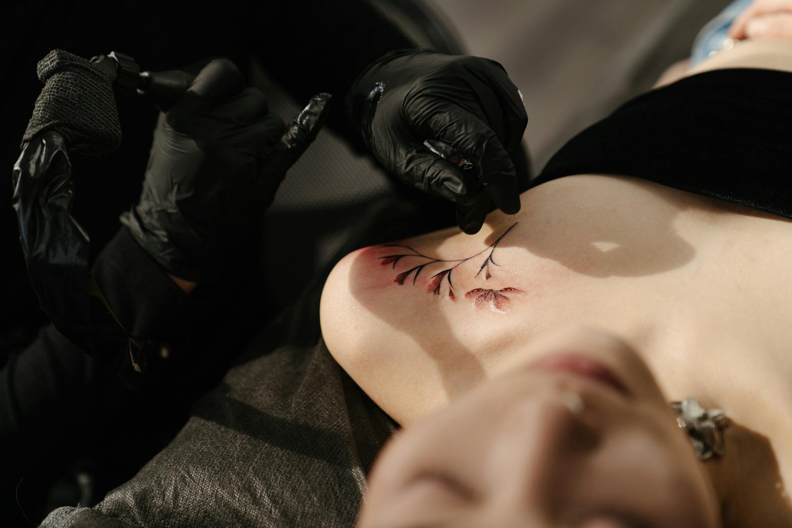 Nahaufnahme einer Frau, die ein Blumen-Tattoo im Schulter-Schlüsselbein-Bereich gestochen bekommt.
