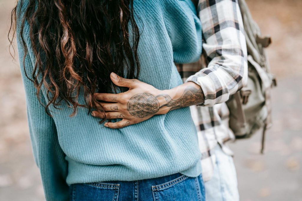 Eine Person hält eine Frau im Arm, auf dem Handrücken ist ein Tattoo zu sehen. Das Tattoo ist im japanischen Stil und zeigt ein Muster.