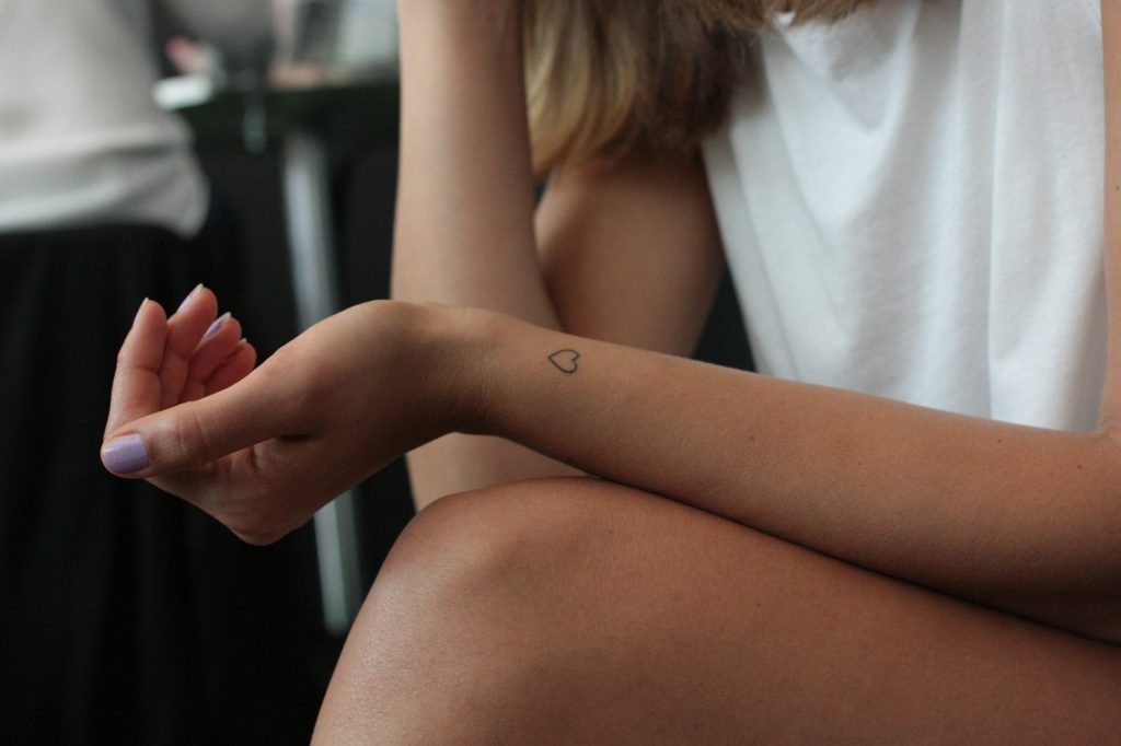Nahaufnahme eines Armes mit einem kleinen, dezenten Herz-Tattoo am Handgelenk.