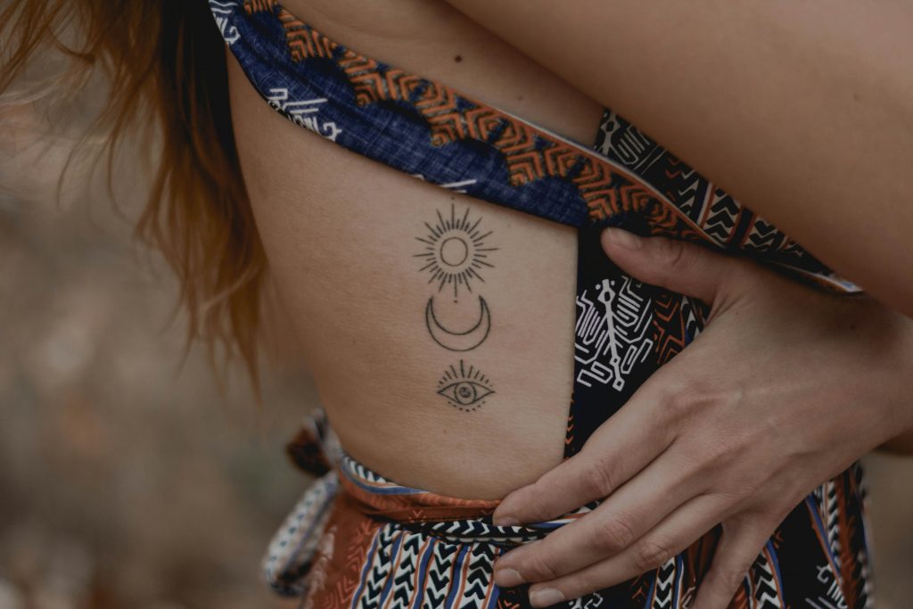 Nahaufnahme einer rothaarigen Frau, die ein Tattoo im seitlichen Rippenbereich zeigt.