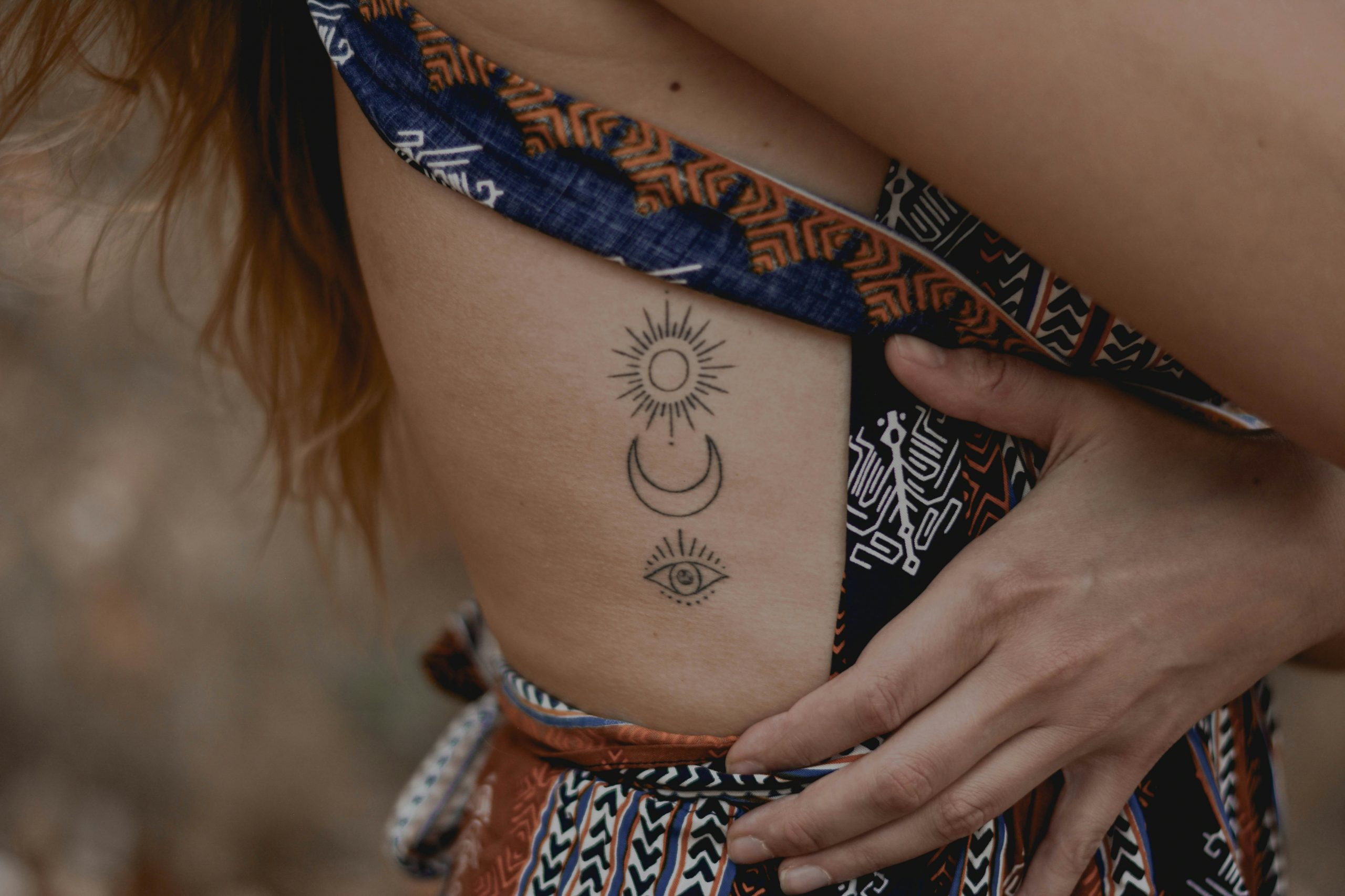 Nahaufnahme einer rothaarigen Frau, die ein Tattoo im seitlichen Rippenbereich zeigt.