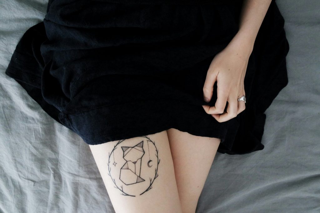 Nahaufnahme einer Frau, die ein stilisiertes Fuchs-Tattoo im Fineline-Stil auf dem Oberschenkel hat.