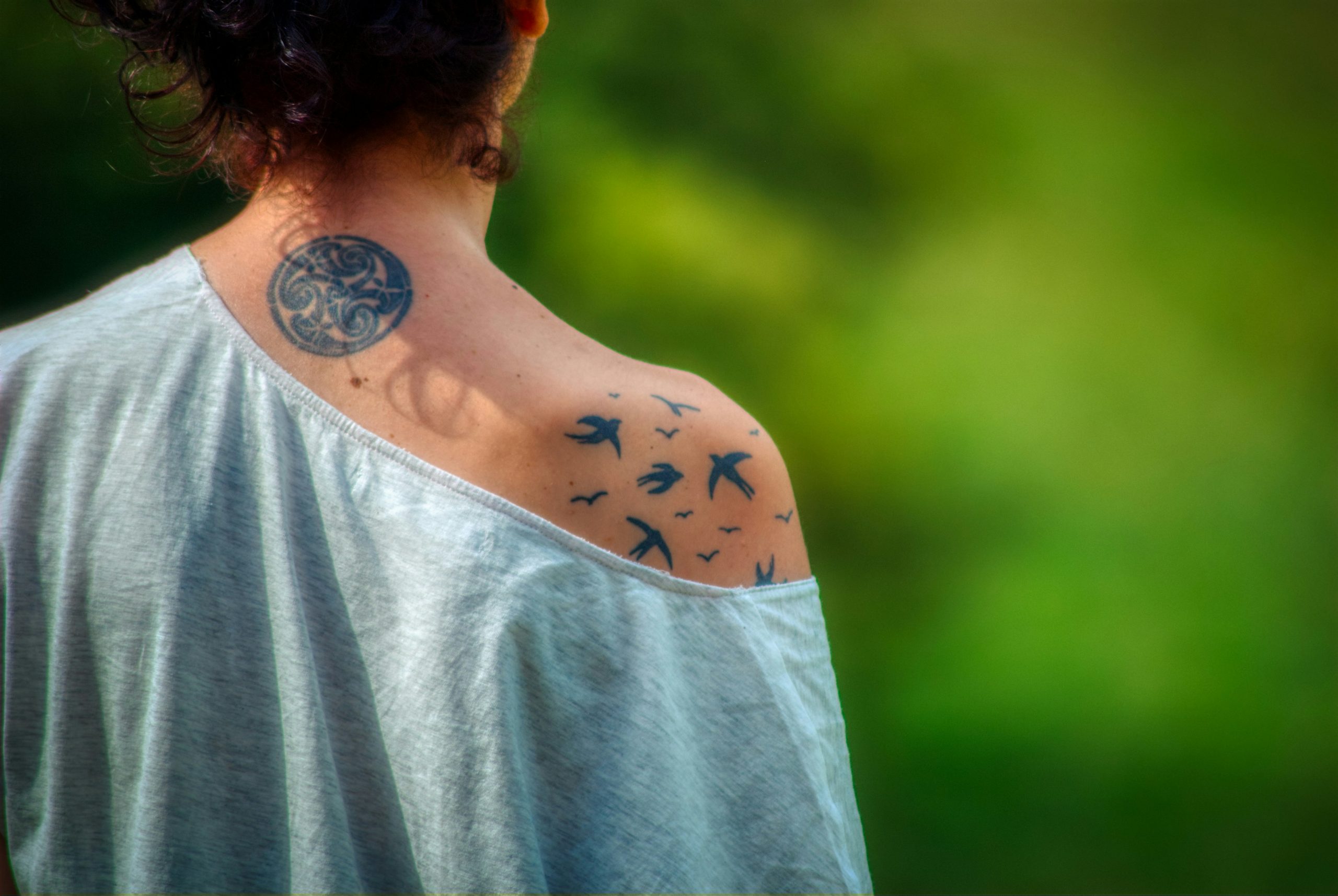 Foto einer Frau, die von hinten zu sehen ist. Auf Schulter und Nacken sind Tattoos zu sehen.