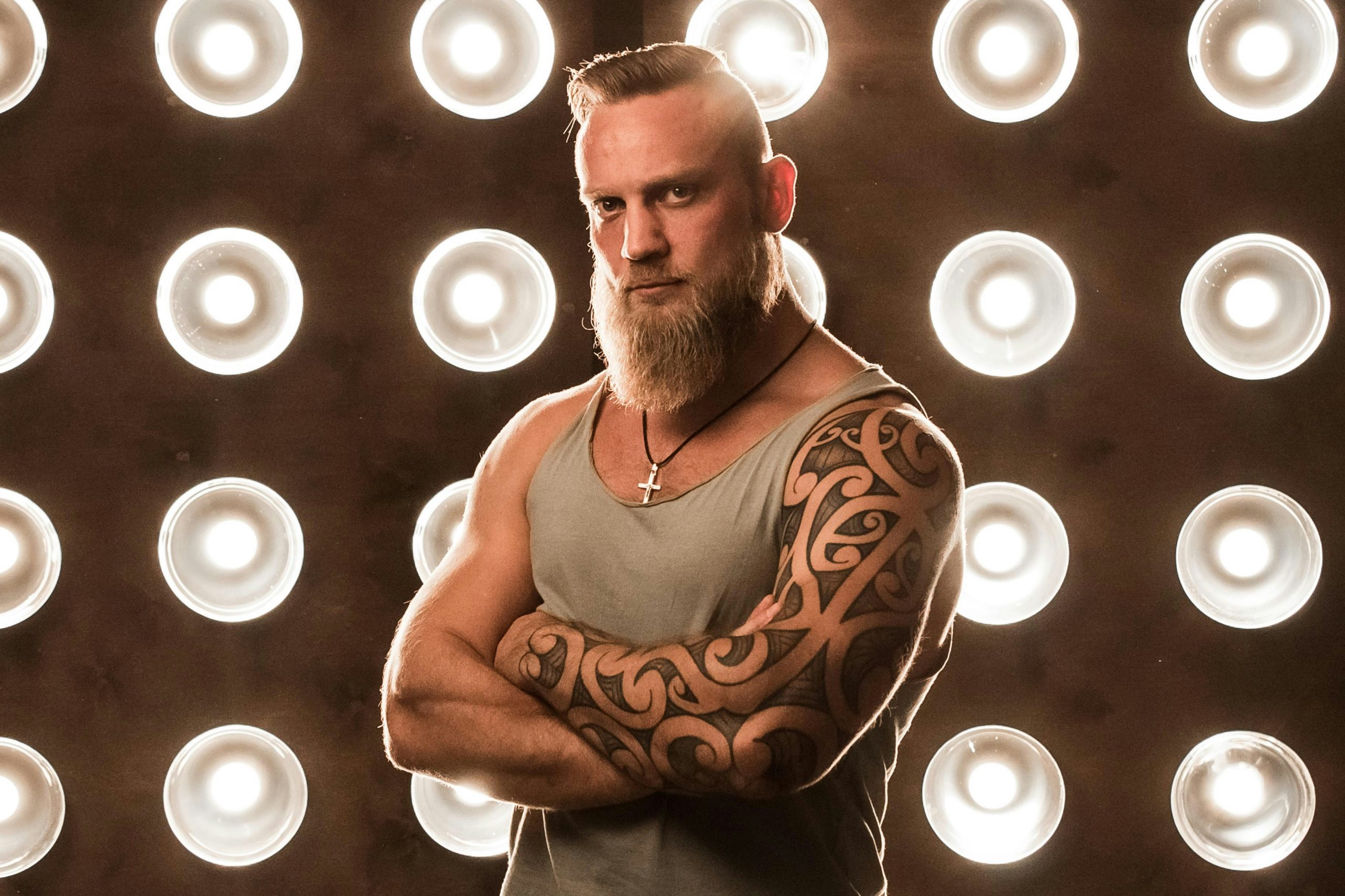 Ein blonder Mann mit Sleeve-Tattoo steht vor einer Wand voller Lampen. Das Tattoo zeigt keltische Ornamente.
