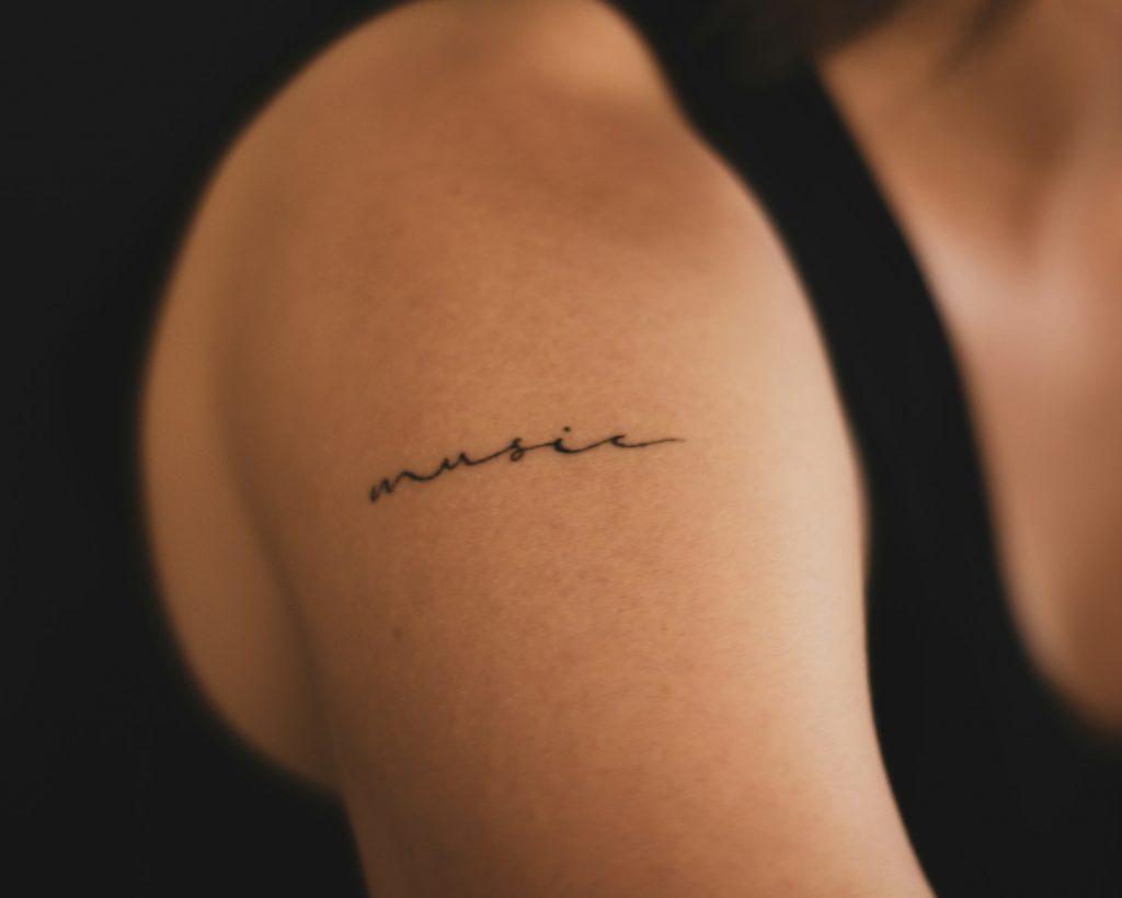 Nahaufnahme eines Oberarm-Tattoos im Schriftzug- oder Lettering-Stil.