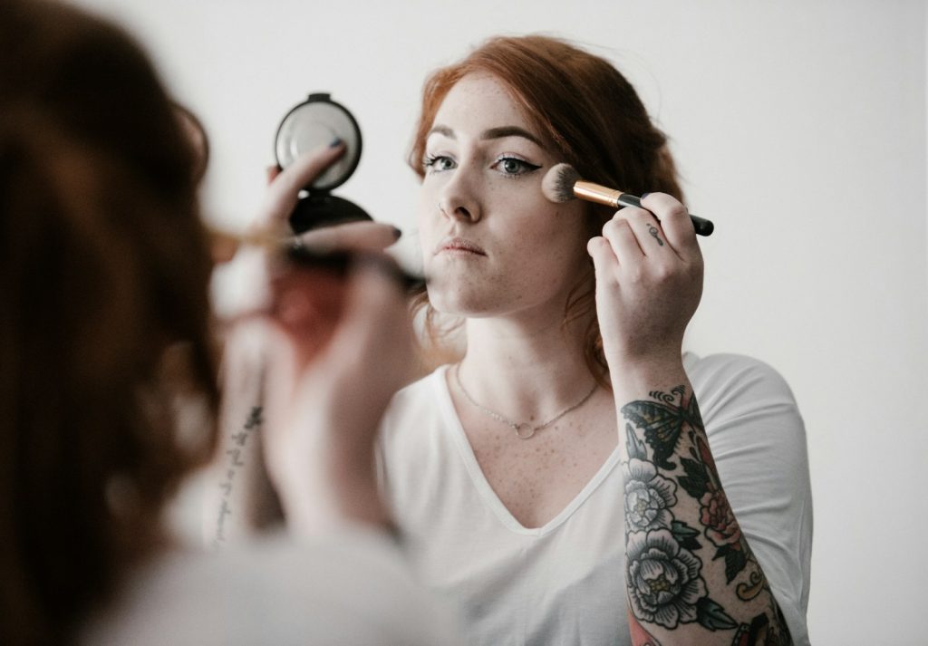 woman using makeup. On her Forearm ist a big tattoo with flowers and butterflies.