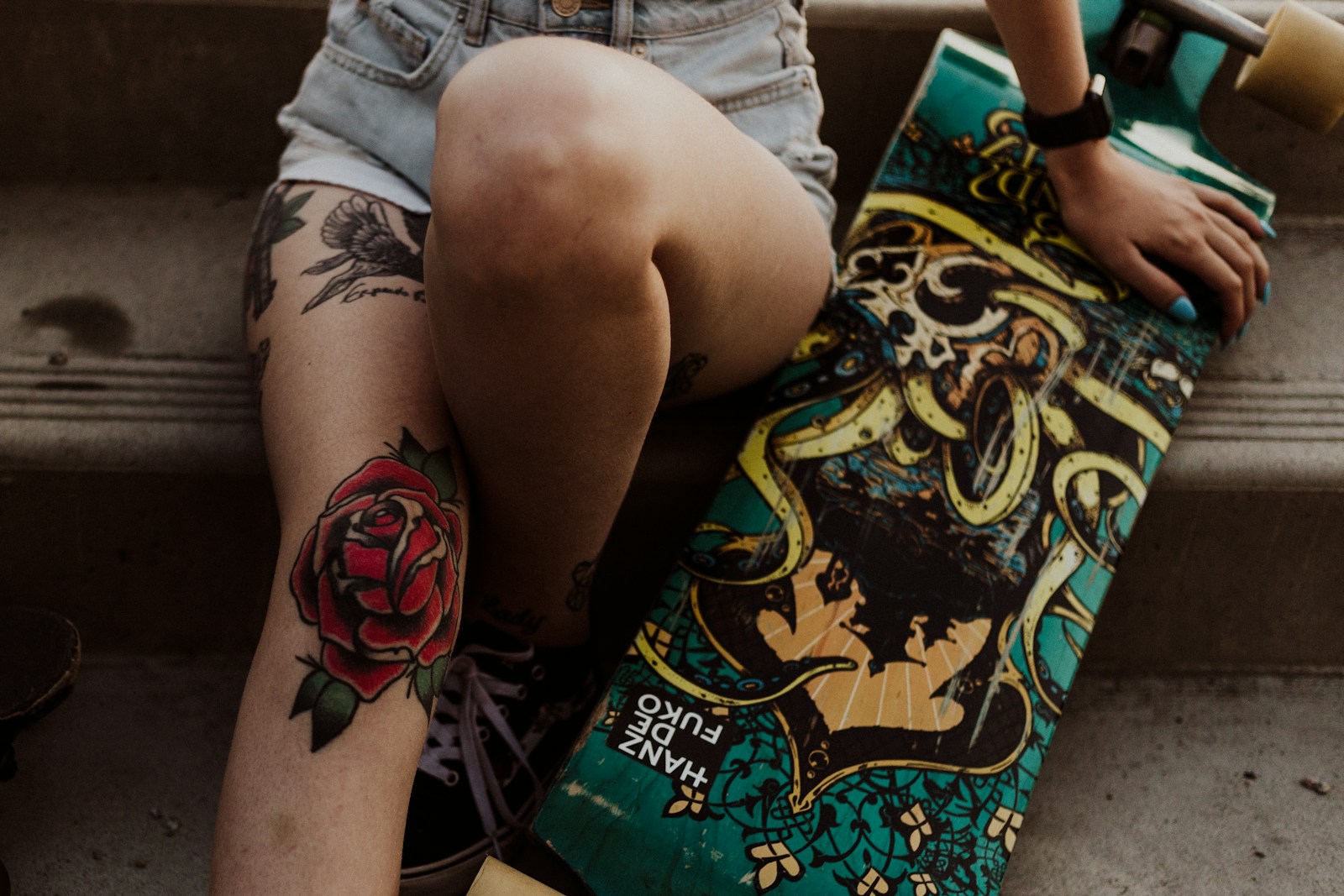 woman holding longboard, a red rose is tattoed on her knee.