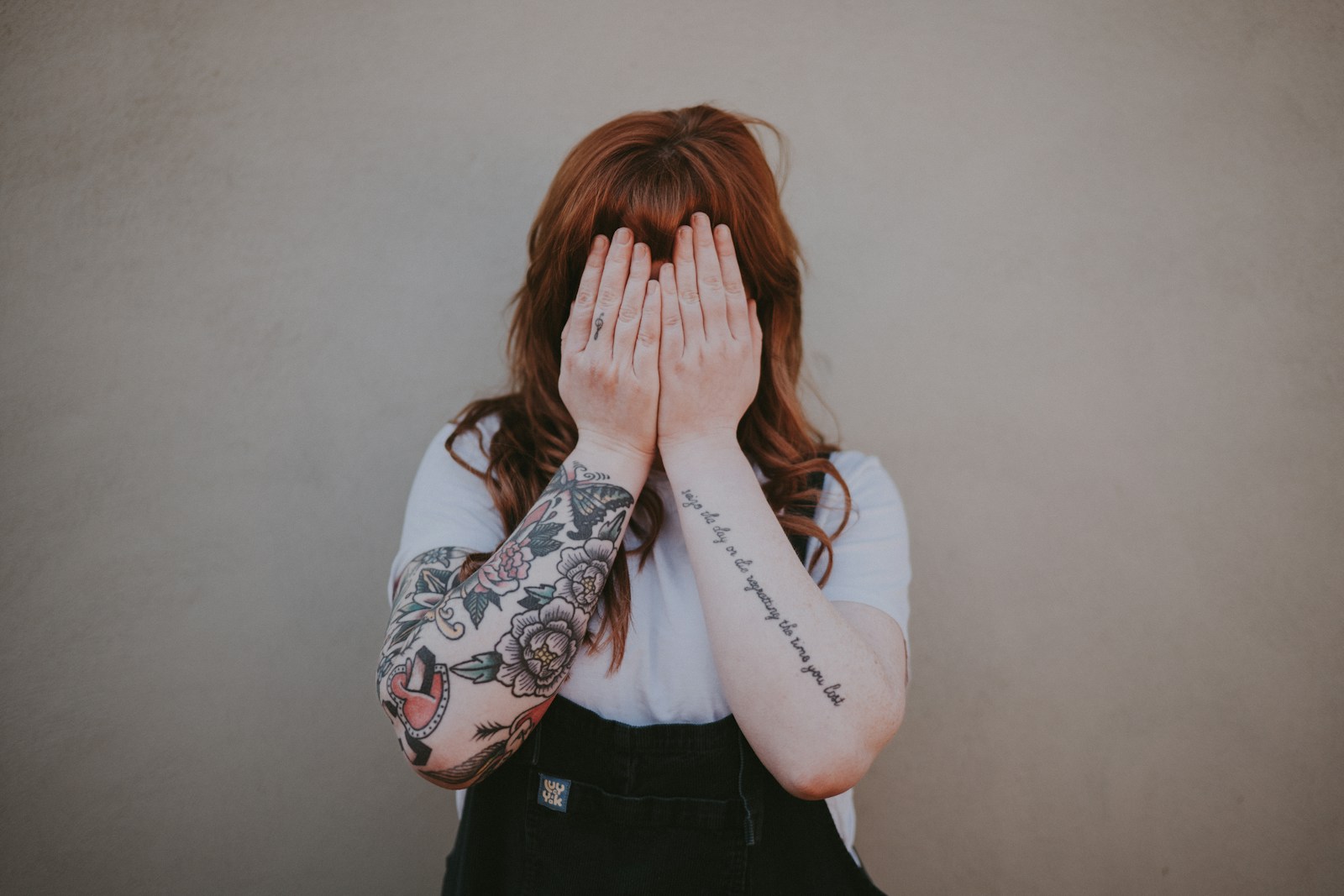 woman covering her face in front of wall_Arm-Tattoo