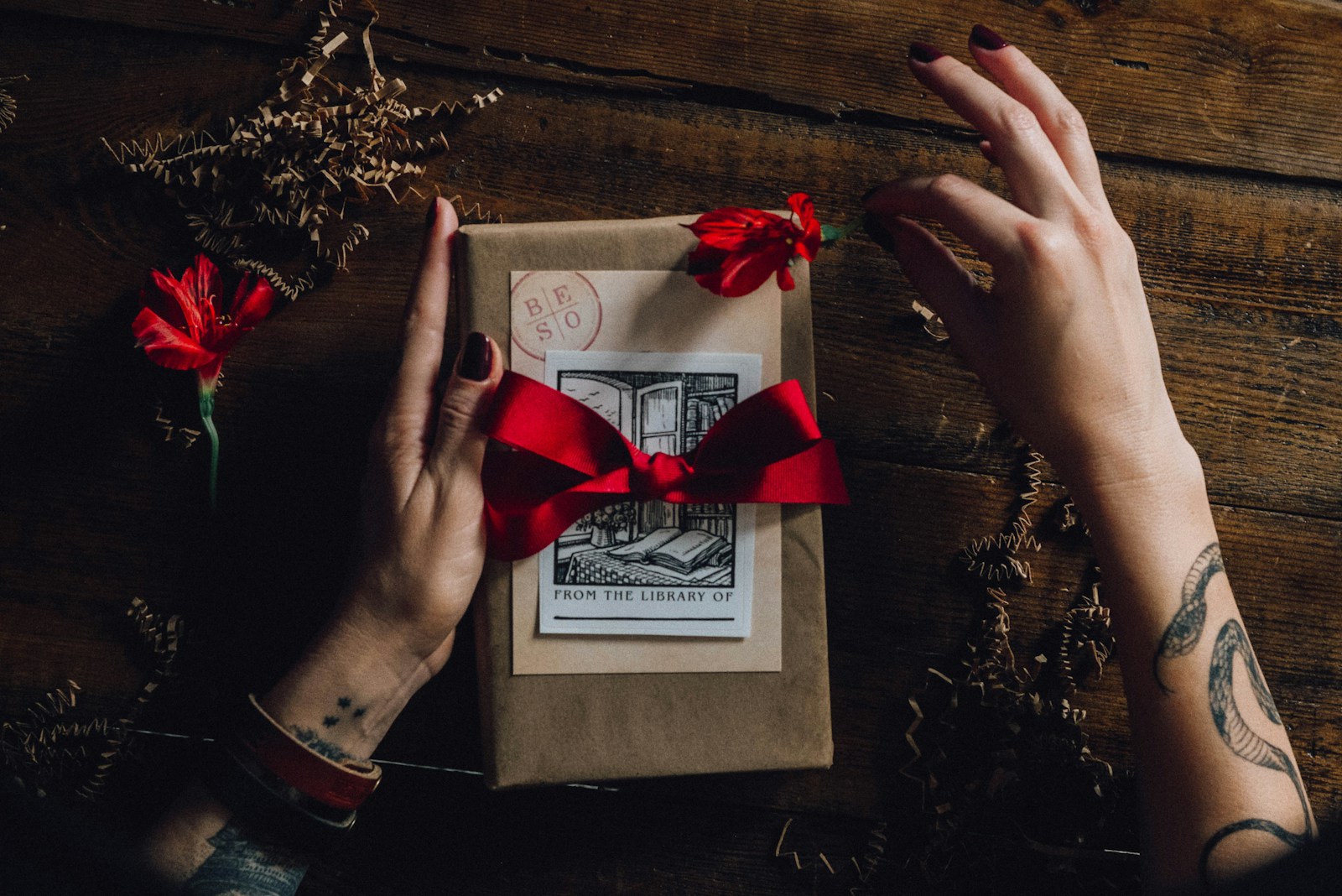 red ribbon on white greeting card. Person with Tattoos on forearms presents a gift-Coupon.