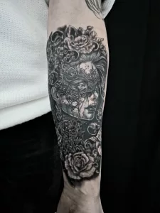 Nahaufnahme eines Unterarms mit einem großen Black-and-Grey-Tattoo. Porträt einer maskierten Frau im venezianischen Stil, von Blumen umgeben.