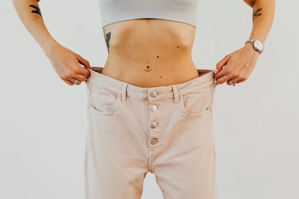Close-up of a woman holding oversized pants at her waist, showcasing significant weight loss.