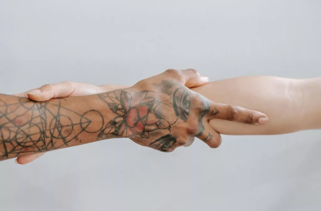 Close-up of diverse hands with tattoos holding each other, symbolizing unity and support.