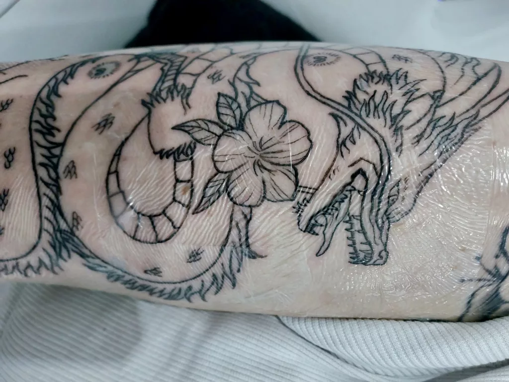 Nahaufnahme eines Unterarms. Auf dem Arm ist ein Drachen-Tattoo zu sehen. Das Tattoo ist mit Tattoo-Folie überklebt.