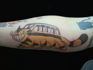 Nahaufnahme eines Unterarms mit farbigem Tattoo. Das Tattoo zeigt den Catbus von Studio Ghibli aus Mein Nachbar Totoro.