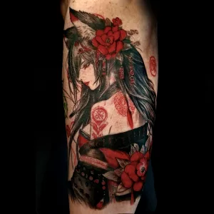 Nahaufnahme eines Oberarm-Tattoos. Das Tattoo ist farbig in schwarz und Rottönen und zeigt einen weiblichen Fuchsdämon im Halbprofil.