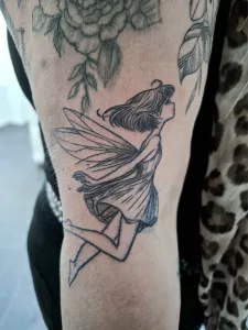 Nahaufnahme eines kleinen Oberarm-Tattoos. Eine kleine fliegende Elfe in black-and-grey.