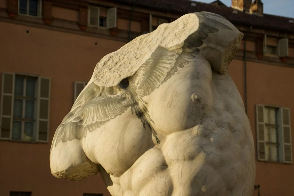 Nahaufnahme einer Statue eines männlichen Oberkörpers ohne Kopf und Arme mit einem symmetrischen Tattoo auf der Brust.