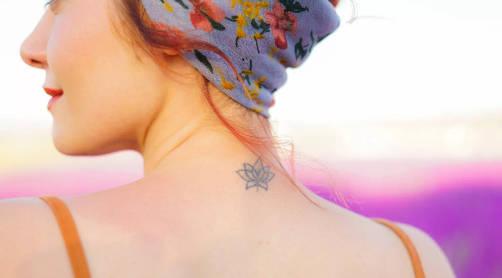 Close-up of woman with floral headband and neck tattoo in sunny outdoor setting.