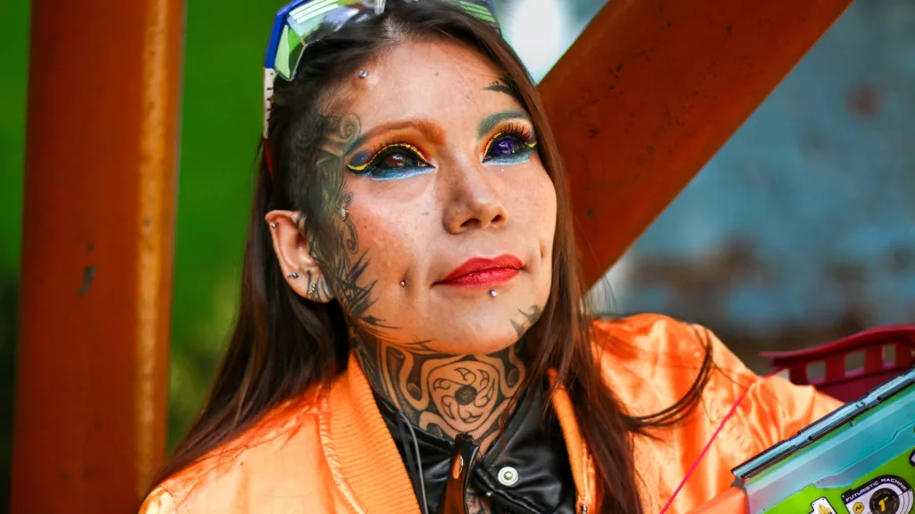 Vivid portrait of a tattooed woman with colorful makeup and piercings outside.