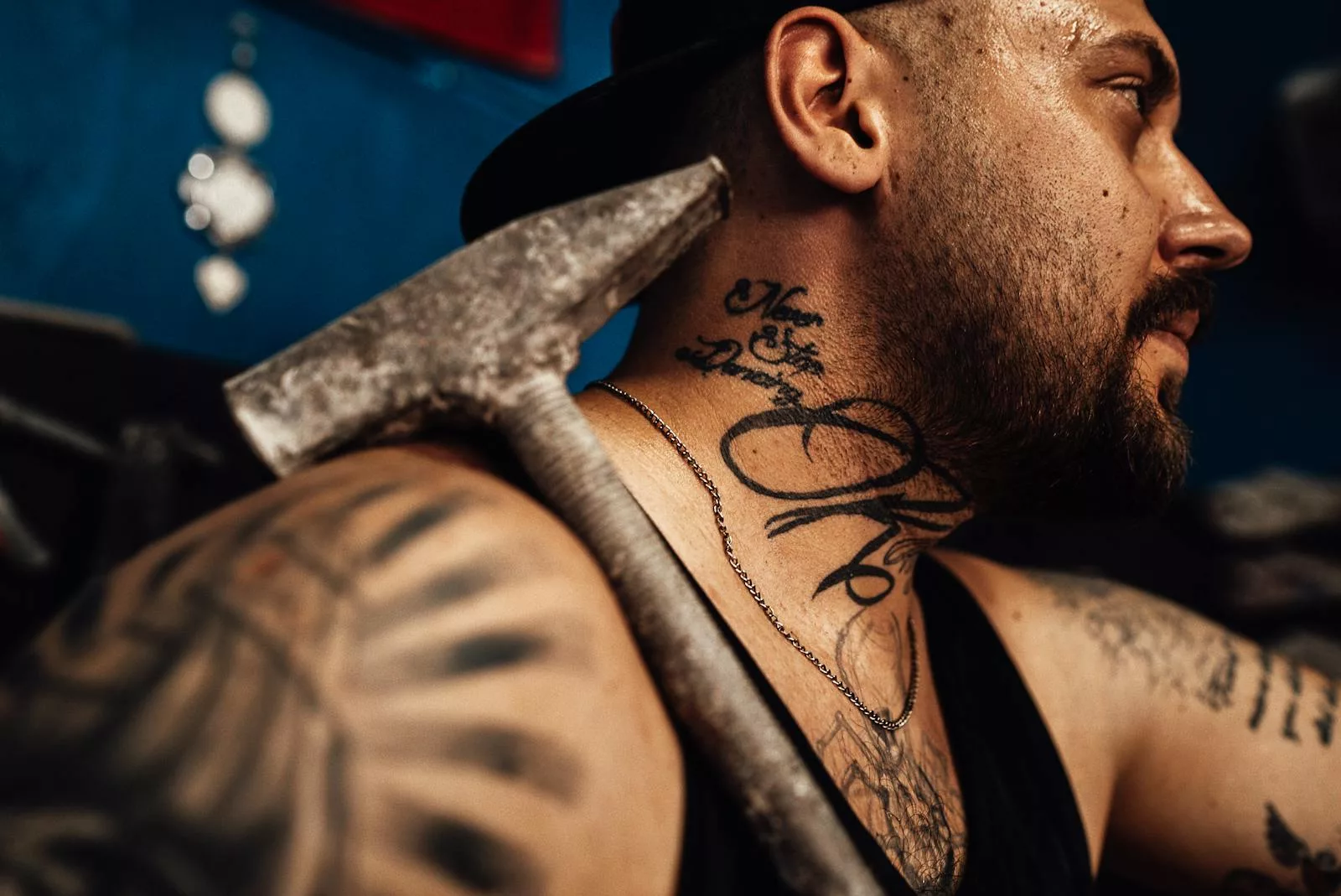 Close-up portrait of a tattooed man with a beard holding a hammer, showcasing detailed facial hair and tattoos.