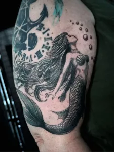 Nahaufnahme eines Oberarm-Tattoos: Meerjungfrau im black-and-grey-Stil.