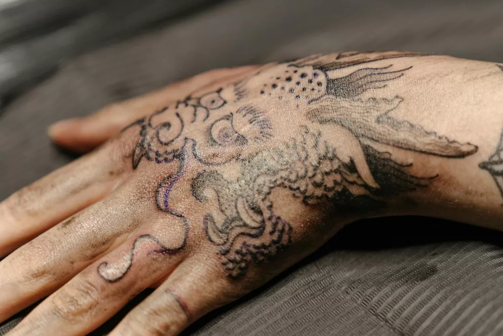 Close-up view of a detailed hand tattoo featuring a dragon design in a tattoo studio.