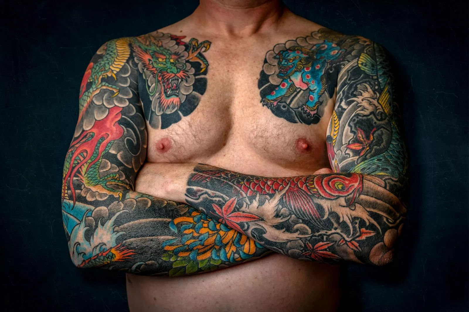 Close-up of a shirtless man with colorful sleeve tattoos and chest art.