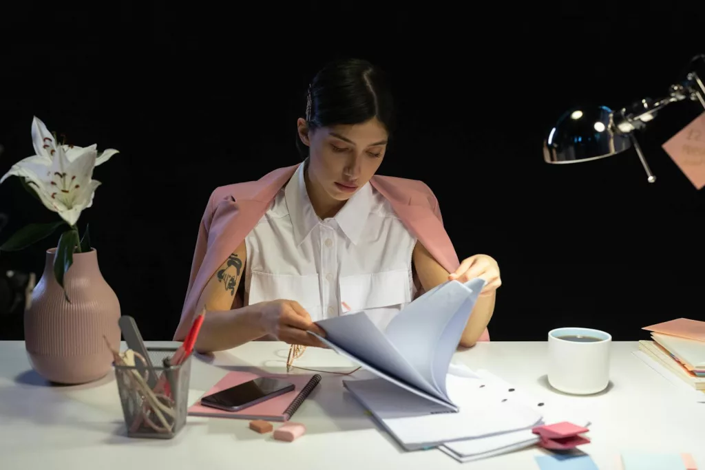 A professional woman focused on reading documents at her desk in a modern office setting.