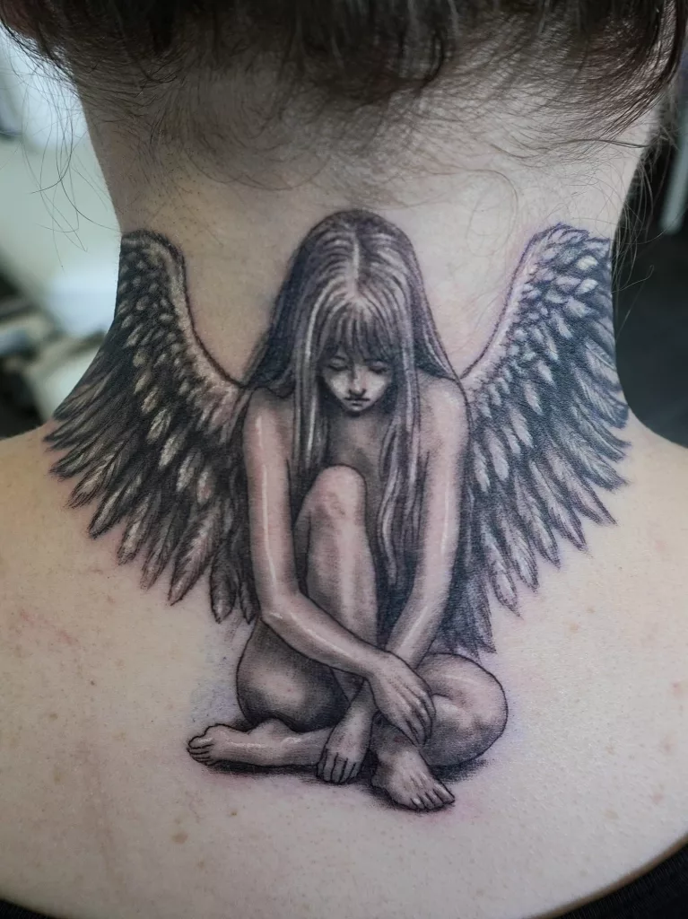 Nahaufnahme eines Nacken-Tattoos in Black and Grey. Ein sitzender Engel mit ausgebreiteten Flügeln.