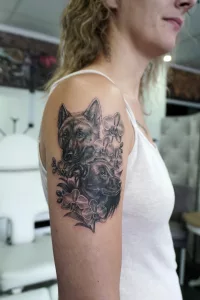 Ein Oberarm-Tattoo in Black and Grey. Zwei Hundeköpfe zwischen Orchideen.