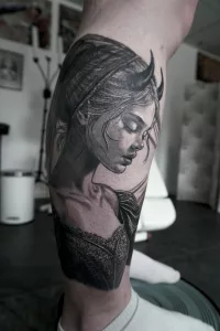 Nahaufnahme eines Unterschenkel-Tattoos in Black and Grey. Eine junge Dämonin im Barockkleid mit kleinen Hörnern auf dem Kopf.
