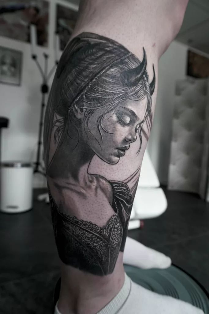 Nahaufnahme eines Unterschenkel-Tattoos in Black and Grey. Eine junge Dämonin im Barockkleid mit kleinen Hörnern auf dem Kopf.
