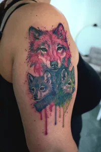 Nahaufnahme eines bunten Watercolor-Oberarm-Tattoos. Eine Wölfin mit zwei Jungen.