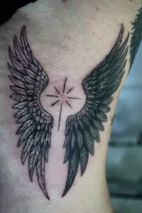 Nahaufnahme eines Oberarms mit Tattoo. Zwei Flügel, die einem Stern umschließen.