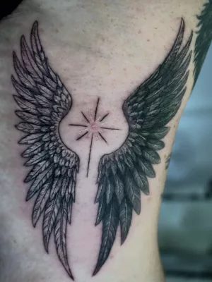 Oberarm-Tattoo-Flügel-Stern-black-and-grey Nahaufnahme eines Oberarms mit Tattoo. Zwei Flügel, die einem Stern umschließen.