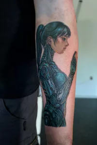 Nahaufnahme eines farbigenUnterarm-Tattoos. Ein Mecha-Mädchen im seitlichen Profil.
