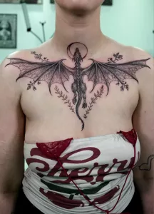 Eine Frau mit einem großen Brust-Tattoo in black and grey, das einen fliegenden Drachen zeigt.