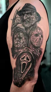 Nahaufnahme eines Oberarm-Tattoos in black and grey. Das Tattoo zeigt Horror-Ikonen wie Freddy Krueger und Michael Meyers.