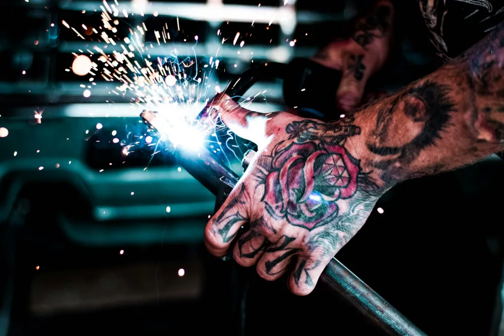 man with tattoo on his hand welding metal rod