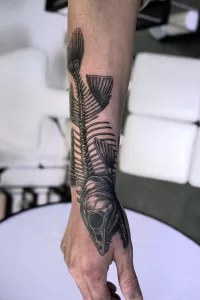 Nahaufnahme eines großen Fischgräten-Tattoos am Unterarm.