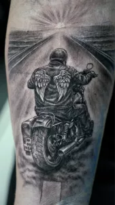 Nahaufnahme eines Tattoos in black and grey. Ein Motorradfahrer fährt auf den Sonnenuntergang zu.