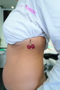 Nahaufnahme eines Unterbrust-Tattoos, das zwei knallrote Kirschen zeigt.