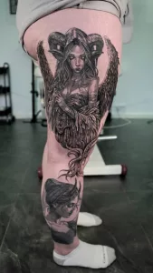Oberschenkel-Tattoo in Black and Grey. Das Motiv zeigt eine geflügelte Dämonin mit gewundenen Hörnern auf dem Kopf.