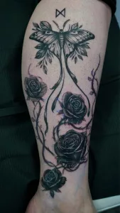 Nahaufnahme eines Unterschenkel-Tattoos in Black and Grey. Schwarze Rosen und eine große Motte.