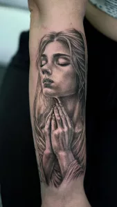 Nahaufnahme eines Unterarm-Tattoos. Das Tattoo zeigt das Porträt einer betenden Frau in black and grey.