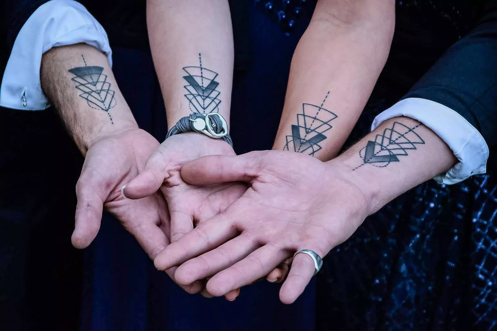 A detailed view of two pairs of hands with matching geometric tattoos, symbolizing unity.