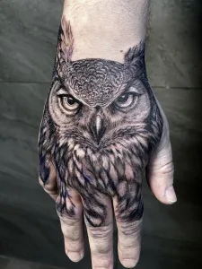 Nahaufnahme eines Handrücken-Tattoos in Black and Grey. Das Motiv zeigt eine Eule im Porträt.